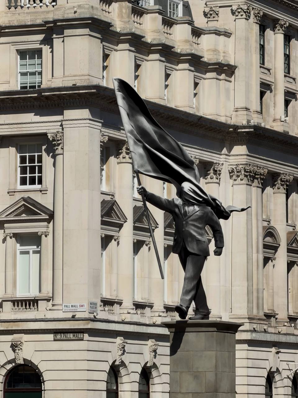 Banksy’s Waterloo Place statue showing a suited figure stepping from a plinth while a flag covers his face.