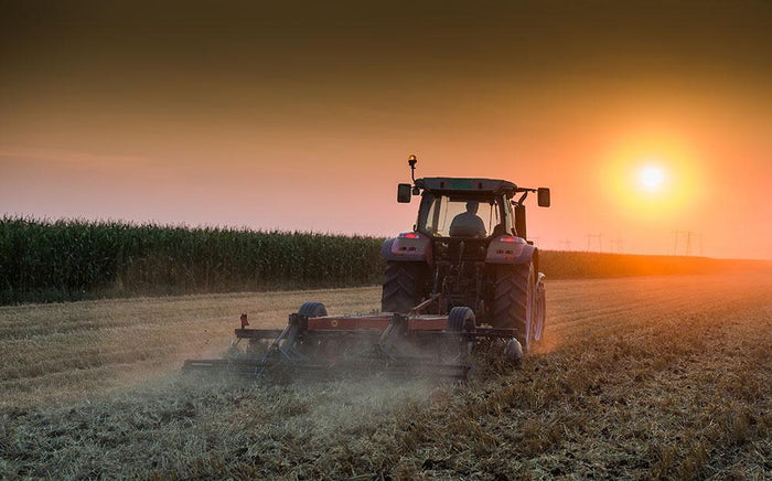 Tractor plowing field at dusk Wall Mural Wallpaper